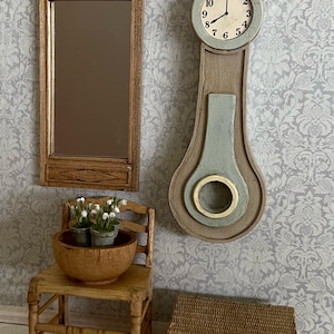May include: A miniature dollhouse scene with a wooden mirror, a clock, a chair, and a wicker basket. The clock is a tall, slender design with a light blue face and a white dial. The chair is made of wood and has a brown bowl on the seat. The basket is brown and has a woven lid. The scene is set against a white and gray floral wallpaper.
