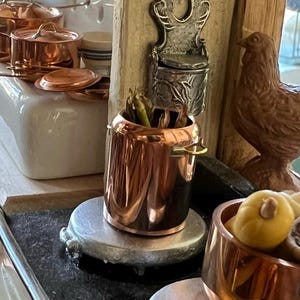 May include: A miniature kitchen set with copper pots and pans, a ceramic stovetop, and a wooden chicken figurine. The set is designed for a 1:12 scale dollhouse.
