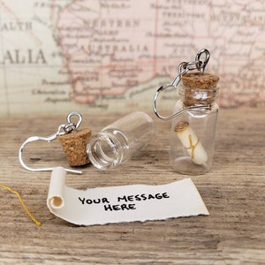 May include: A pair of silver earring with a small glass bottle charm. Each bottle contains a rolled up piece of paper with the text "Your message here".