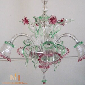May include: A clear glass chandelier with pink and green glass flowers. The chandelier has five lights and is decorated with a floral motif.