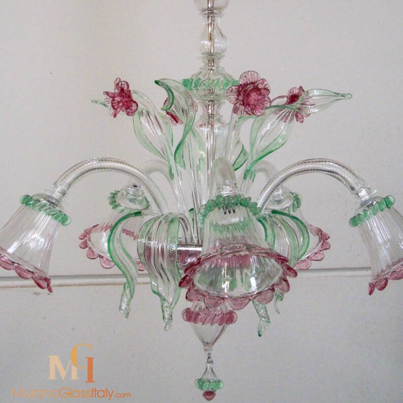May include: A clear glass chandelier with pink and green glass flowers. The chandelier has five lights and is decorated with a floral motif.
