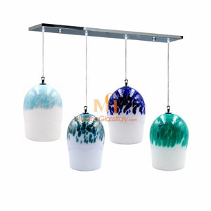 Può includere: Un lampadario moderno con quattro paralumi in vetro. I paralumi sono bianchi con motivi macchiati di blu, verde e nero. Il lampadario è sospeso da una barra cromata.