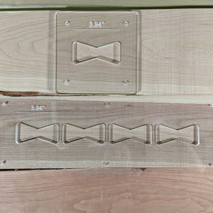 May include: Two clear plastic templates for woodworking. The top template has a single bowtie shape cutout, labeled "3.94". The bottom template has six bowtie shape cutouts, also labeled "3.94".