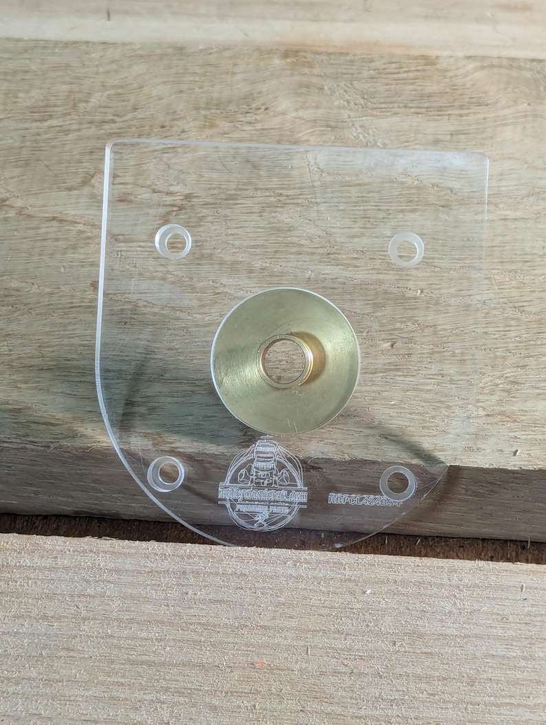 May include: A clear plastic template with four holes and a brass ring in the centre. The template has the text "The Router Workshop" and "RIP-CLASSIC" printed on it.