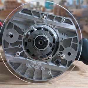 May include: A silver router base with a clear plastic cover. The base has a number "128" and the text "BS7.5 MRP23EVS" printed on it.