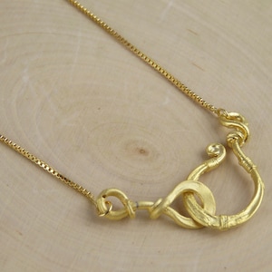 May include: A gold necklace featuring a distinctive, twisted and knotted pendant. The pendant is crafted from thick, textured wire and boasts a simple, elegant design.