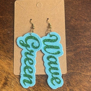 May include: A pair of blue glitter earrings with the words "Green" and "Wave" written in green glitter.