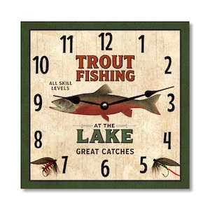 May include: Square wall clock with a green textured border. The clock face features a trout illustration and the words "TROUT FISHING" and "AT THE LAKE". Black clock hands point to the time. Includes fishing flies.