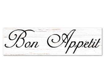 May include: A rectangular wooden sign with a white background and the words "Bon Appétit" in elegant black script. The sign has a rustic, weathered appearance, suggesting a farmhouse or kitchen theme.