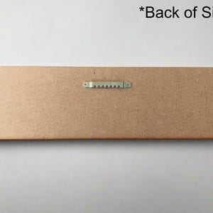 May include: The back of a wooden sign with a metal hanging hook. The sign is brown and has a rough texture.