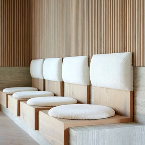 May include: A row of five white cushioned benches with wooden frames, set against a wall of vertical wooden slats.