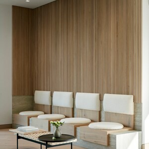 May include: A waiting area with a wooden slat wall and a row of white cushioned benches with wooden bases. A black metal coffee table with a wooden top sits in front of the benches.