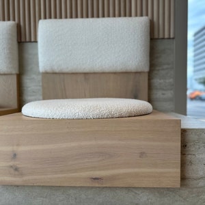 May include: Two white cushioned chairs with wooden frames and a light wood base. The chairs are set against a wall with a light wood paneling and a light gray stone surface.