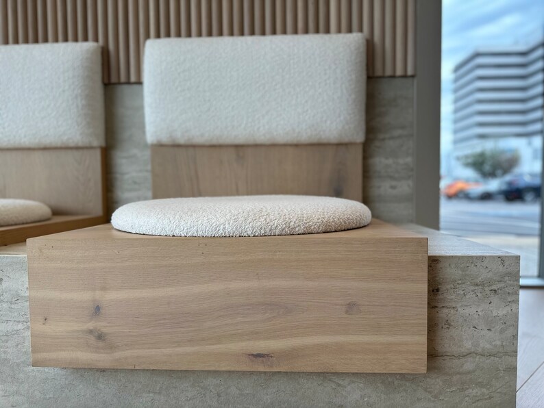 May include: Two white cushioned chairs with wooden frames and a light wood base. The chairs are set against a wall with a light wood paneling and a light gray stone surface.