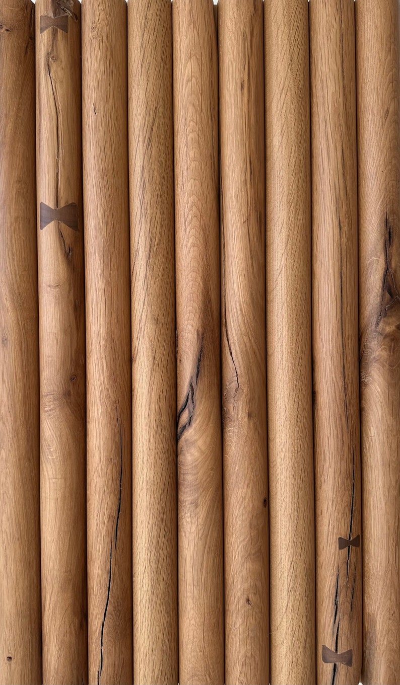 May include: Close-up of a wall made of multiple wooden dowels, each with a unique grain pattern. The dowels are arranged vertically and have a natural brown colour. There are small, dark brown metal accents at the top and bottom of some of the dowels.