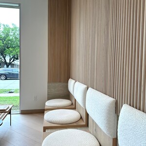 May include: Four white cushioned seats with wooden frames line a wall with vertical wood paneling. The seats are arranged in a row, with the cushions facing the viewer.