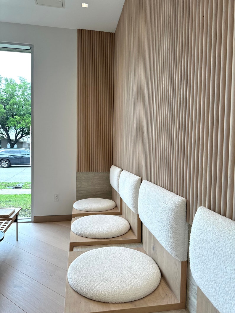 May include: Four white cushioned seats with wooden frames line a wall with vertical wood paneling. The seats are arranged in a row, with the cushions facing the viewer.