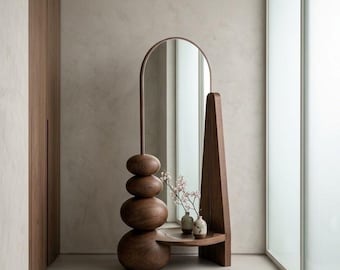 May include: A floor-standing mirror featuring a dark wood frame with a tall arched top. The base consists of four stacked, rounded wooden spheres on one side, connected to a flat shelf holding two small ceramic vases with delicate floral stems.