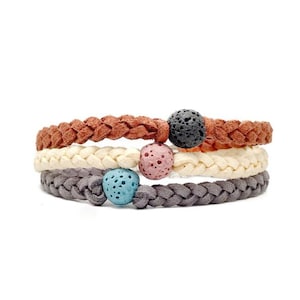 May include: Three braided bracelets with lava rock beads in black, pink, and blue. The bracelets are made of brown, white, and gray cord.