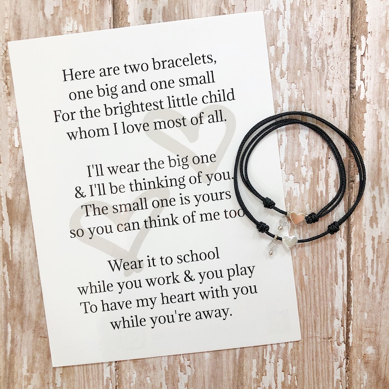 May include: Two black string bracelets with silver heart charms. A card with a poem reads: "Here are two bracelets, one big and one small For the brightest little child whom I love most of all. I'll wear the big one & I'll be thinking of you. The small one is yours so you can think of me too Wear it to school while you work & you play To have my heart with you while you're away."