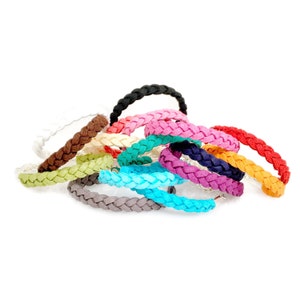 May include: A collection of braided bracelets in various colors, including black, brown, pink, blue, green, and white. The bracelets are made of a soft, pliable material and are stacked on top of each other.