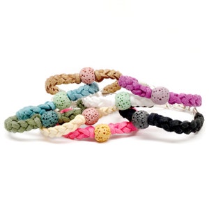 May include: A set of braided bracelets with lava stone beads in various colors, including pink, green, brown, black, and white. The bracelets are made of braided suede and have a silver metal clasp.