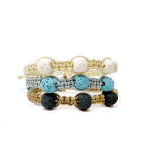May include: Three layered bracelets with lava rock beads. The top layer has white beads, the middle layer has blue beads, and the bottom layer has black beads.