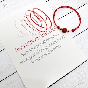 May include: Red string bracelet with a red lava stone bead and gold beads. The bracelet is on a white background with text that reads "Red String Bracelet Wear to ward off negative energy and bring about good fortune and wealth."