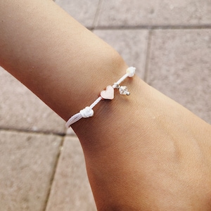 May include: A white string bracelet with a rose gold heart charm and a clear crystal charm.