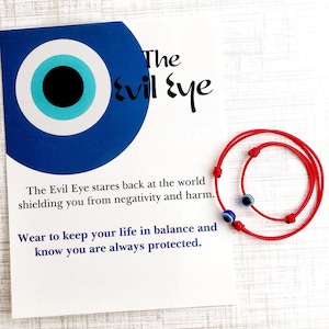 Puede incluir: Pulsera de cuerda roja con un amuleto de ojo turco azul. El mal de ojo mira al mundo protegiéndote de la negatividad y el daño. Úsala para mantener tu vida en equilibrio y saber que siempre estás protegido.