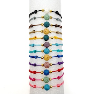 May include: A set of 12 bracelets with colorful cords and lava rock beads. Each bracelet has a different color cord and a single lava rock bead in a variety of colors.