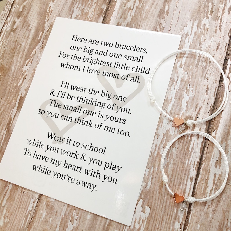 May include: Two white string bracelets with rose gold heart charms. The bracelets are accompanied by a card with a poem about wearing one bracelet and thinking of the person who wears the other.