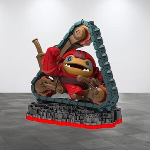 May include: A red and brown toy figure of a creature with a large head and a small body, riding a toy tank with green tracks. The figure is posed with its arms raised and its mouth open. The tank is on a gray and black base.