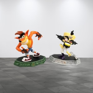 May include: Two action figures of video game characters. The first figure is orange and yellow with blue jeans and red and white shoes, posed on a green base. The second figure is yellow, black, and white, on a silver base.