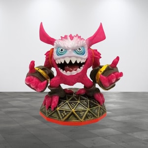 May include: A pink and white monster toy with horns and a toothy grin, standing on a gold and black base. The monster has blue eyes and is wearing black and gold armor.