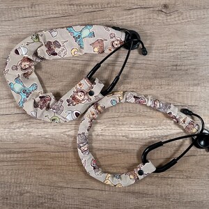 May include: Two stethoscope covers with a cartoon character print. The covers are beige with a variety of colorful characters. One cover is a long tube, and the other is a shorter, circular cover.