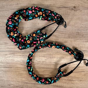 May include: Two stethoscope lanyards with a floral print on a black background. The lanyards are made of fabric and have a black elastic band.