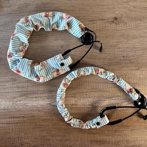 May include: Two stethoscope covers with a Winnie the Pooh print. The covers are made of a soft, stretchy fabric and are designed to fit over a standard stethoscope. The covers are a light blue color with white stripes and feature a repeating pattern of Winnie the Pooh characters.