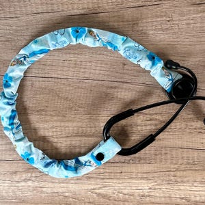 May include: A blue and white stethoscope holder with a floral pattern featuring a princess character. The holder is made of fabric and has a black button.