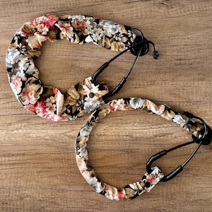 May include: Two black stethoscope holders with a floral pattern. The pattern features red, gold, and white flowers on a black background.