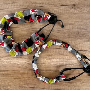 May include: Two stethoscope covers with a black and white checkered pattern and a green and red cartoon character print. The characters are wearing red Santa hats.
