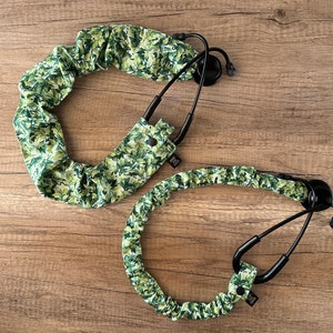 May include: Two stethoscope covers made of green and white fabric with a leafy pattern. The covers are designed to fit around the stethoscope tubing and have a button closure.