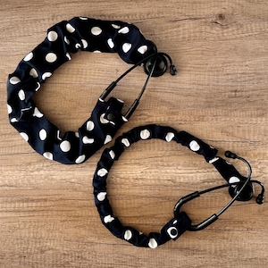 May include: Two black and white polka dot stethoscope covers. The covers are made of fabric and have a stretchy fit. The covers are designed to fit over the tubing of a stethoscope.