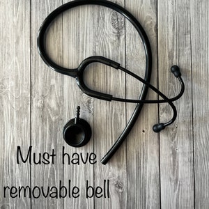 Pu&ograve; includere: Uno stetoscopio nero con un pezzo toracico staccabile, dotato di una campana circolare e un tubo. Il testo "Must have removable bell" &egrave; stampato in lettere nere. Lo strumento medico &egrave; composto da olivette, archetto e un tubo flessibile.