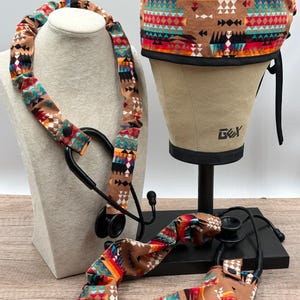 Pu&ograve; includere: Una cuffia chirurgica e due copristetoscopio abbinati con base color marrone chiaro e un motivo geometrico in rosso, arancione, giallo, turchese, nero e bianco. La cuffia ha un bordo nero e le coperture sono tubi in tessuto con bottoni a pressione.