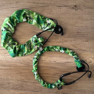 May include: Two stethoscopes with black tubing and ear pieces. The stethoscope tubing is covered in a green and white tropical leaf pattern. The stethoscope covers have a small tag with text.