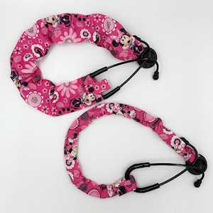 May include: Two pink stethoscope covers with a floral and Minnie Mouse pattern. The covers are padded and have black accents. The stethoscope covers are designed to fit around the stethoscope tubing.