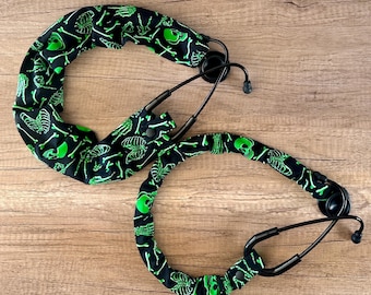 May include: Two black stethoscope lanyards with a green and black skeleton pattern. The lanyards are made of fabric and have a skull and crossbones design.
