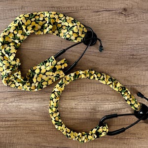 May include: Two stethoscope covers with a lemon print. The covers are made of fabric and have a black background with yellow lemons and green leaves. The covers are designed to fit over the stethoscope tubing.