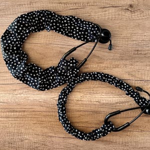 May include: Two black stethoscope covers with a white paw print pattern. The covers are made of fabric and are designed to fit around the stethoscope tubing.